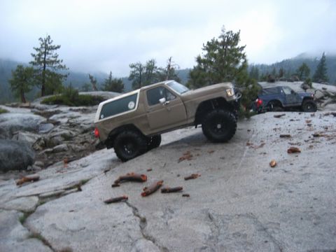 1989 Ford Bronco - A tan 1989 Ford Bronco navigates a steep, rocky terrain, with another off-road vehicle visible behind it.
