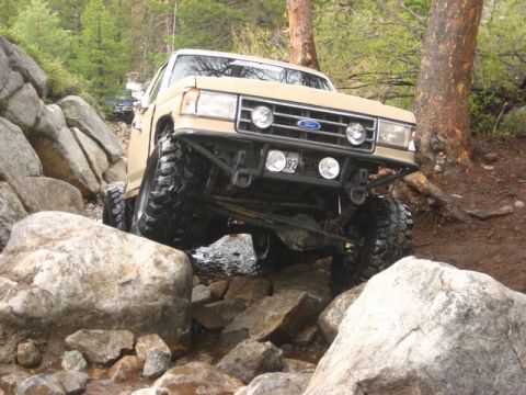 1989 Ford Bronco - This 1989 Ford Bronco is shown tackling a challenging off-road course with significant rock obstacles.