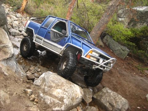1989 Ford Bronco - Modified pickup truck tackling a challenging off-road course with large boulders and water.