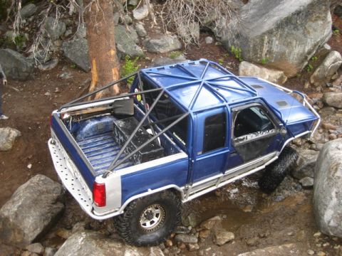 1989 Ford Bronco - This modified pickup truck navigates a rocky, off-road trail with water and large boulders.