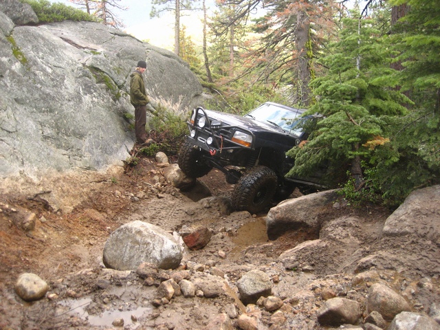 Black lifted Ford Bronco crawling down a muddy rock trail as a man watches