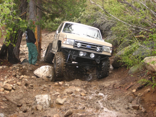 Tan lifted Ford Bronco with white roof descending a wet rocky trail
