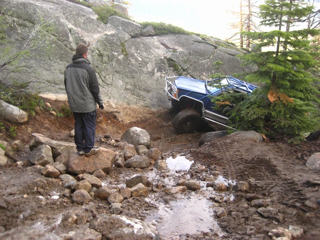 Blue lifted 4x4 rig crawling over boulders on a wet rocky forest trail