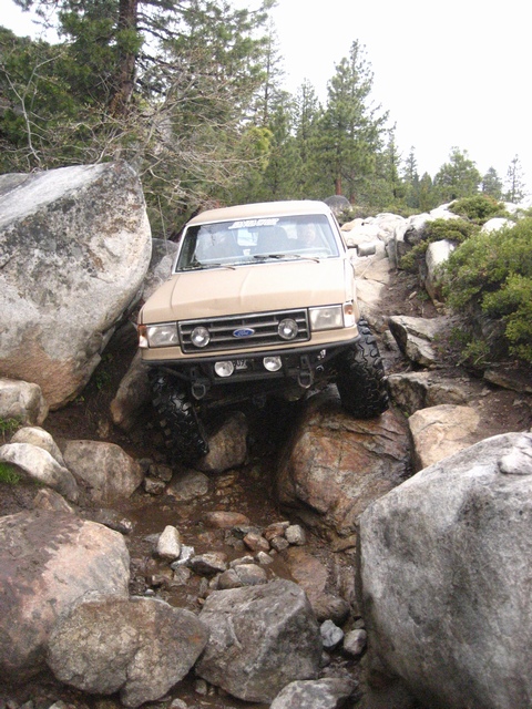 1989 Ford Bronco - This 4x4 is tackling a challenging off-road course with large rocks and uneven terrain.