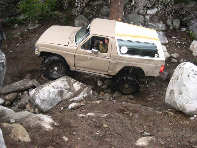 Tan full-size Ford Bronco with white top crawling boulders in a rocky wash