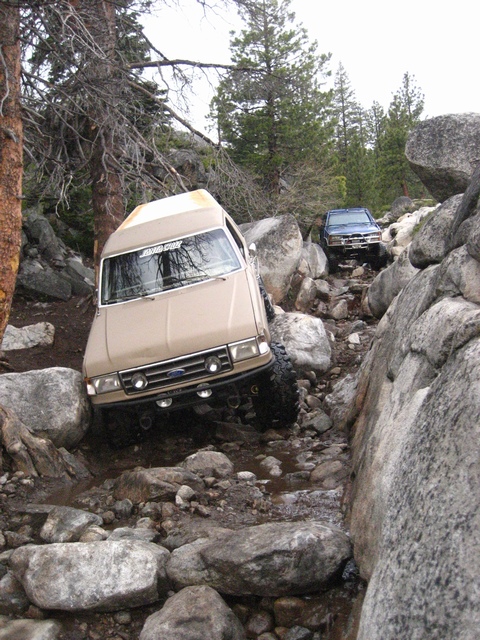1989 Ford Bronco - Two off-road vehicles tackle a challenging rocky path, with one vehicle positioned at an angle on the terrain.