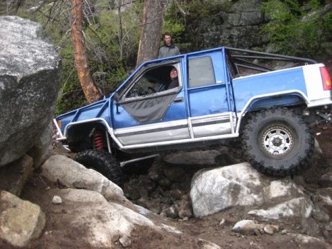 1989 Ford Bronco - A modified blue truck with a roll cage tackles a challenging rocky trail.