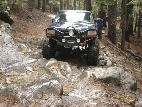 1989 Ford Bronco - This modified SUV navigates a challenging rocky trail through a wooded area.