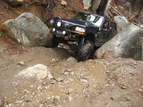 1989 Ford Bronco - A modified Ford Bronco tackles a challenging off-road course with large rocks and mud.