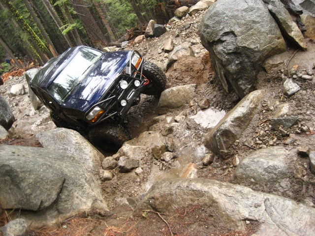 Dark blue off-road SUV crawling over large boulders on a rocky forest trail