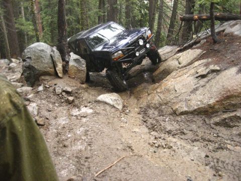 1989 Ford Bronco - Off-road vehicle tackling a challenging rocky and muddy path in a forest.