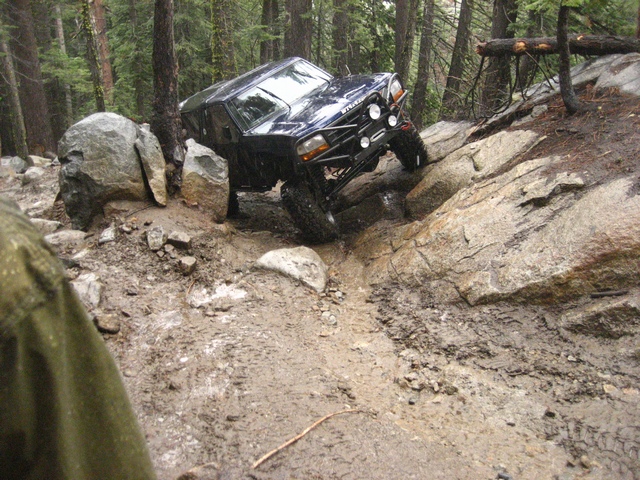 Dark Ford Bronco climbing muddy rocky trail in a forest