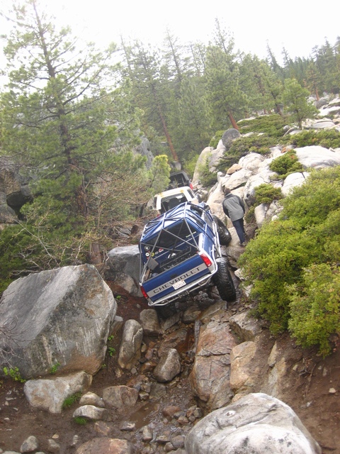 1989 Ford Bronco - Multiple off-road vehicles tackle a challenging rocky trail on a hillside.