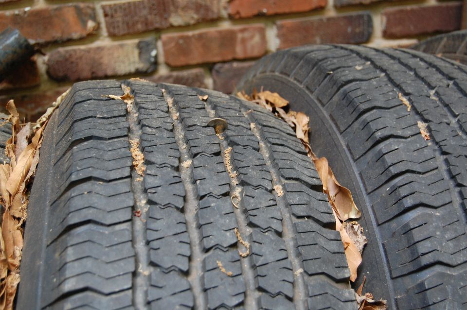 Two old tires with a coin in the tread, against a brick wall.