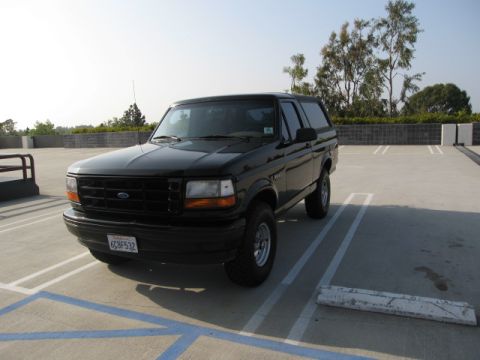 1986 Ford Bronco - A black two-door Ford Bronco is parked in a rooftop parking lot with a clear sky overhead. The vehicle is angled towards the camera, showin…