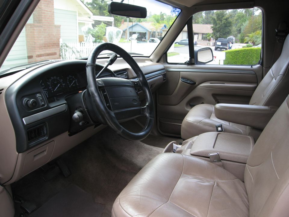 Interior of a tan Ford Bronco, showing seats, steering wheel, dashboard, and view out the window.