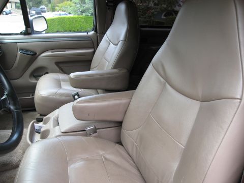 1986 Ford Bronco - The interior of a tan SUV shows two front bucket seats with armrests and a center console. The driver's side door panel and steering wheel…
