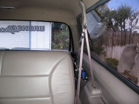 1986 Ford Bronco - Interior view of a vehicle's rear passenger side, showing a tan leather seat and a seatbelt hanging from the ceiling. A sticker with the wo…