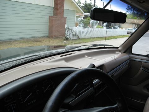 1986 Ford Bronco - Interior view of a classic vehicle's dashboard, steering wheel, and windshield looking out onto a residential street with a white picket fe…