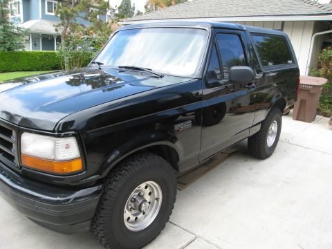 1986 Ford Bronco - A black Ford Bronco is parked in a driveway in front of a house. The vehicle is shown from a 3/4 front angle, highlighting its side profile…