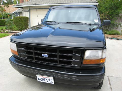 1986 Ford Bronco - Front view of a black Ford Bronco parked in a driveway with a house and trees in the background. The vehicle has a California license plate…