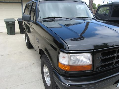 1986 Ford Bronco - A black Ford Bronco is parked in a driveway next to two green trash cans. The vehicle is viewed from the front three-quarter angle, showing…