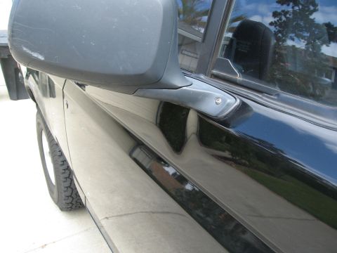 1986 Ford Bronco - Close-up view of the driver's side door and side mirror of a black SUV. The side mirror housing shows some scuff marks and scratches.