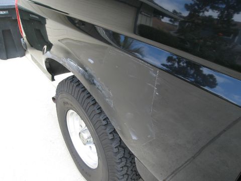 1986 Ford Bronco - A close-up side view of the rear fender and tire of a black vehicle. The fender shows significant scratching and what appears to be body fi…