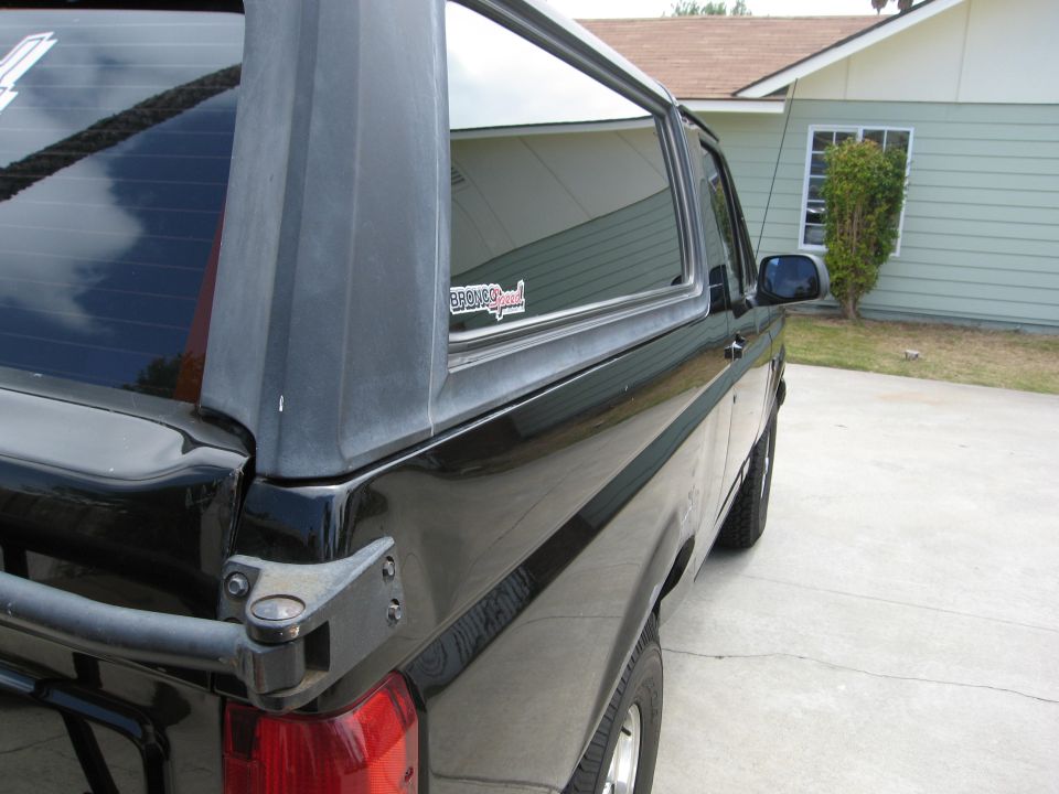 Black Ford Bronco rear passenger side view, parked on concrete driveway.