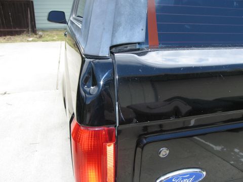 1986 Ford Bronco - The rear driver's side corner of a black Ford pickup truck is shown, with a dented tailgate and a damaged taillight. The vehicle is parked…