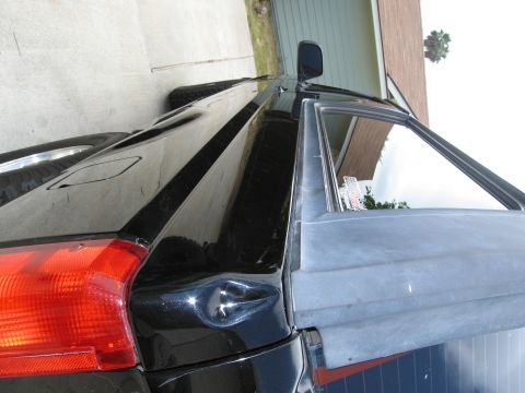 1986 Ford Bronco - The rear driver's side of a black vehicle is shown with a red taillight and a dent on the body panel. The vehicle is parked on a concrete s…
