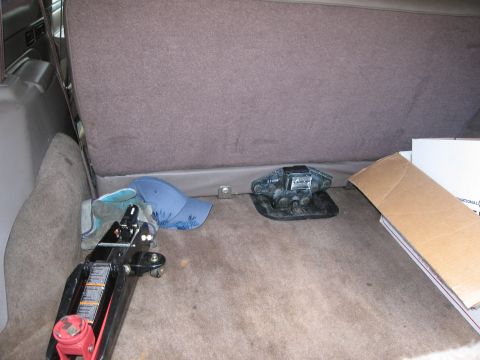 1986 Ford Bronco - The cargo area of an SUV shows a car jack, a blue baseball cap, and a black trailer hitch.