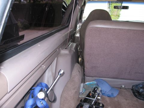 1986 Ford Bronco - The interior of a vehicle shows the rear cargo area with a blue tie-down strap and a lug wrench on the left, and a folded rear seat with a…