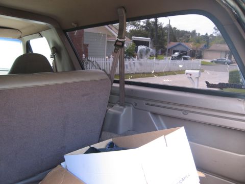 1986 Ford Bronco - Interior view of the rear passenger area of a Ford Bronco, looking out the side window at a suburban street. A cardboard box is visible in…