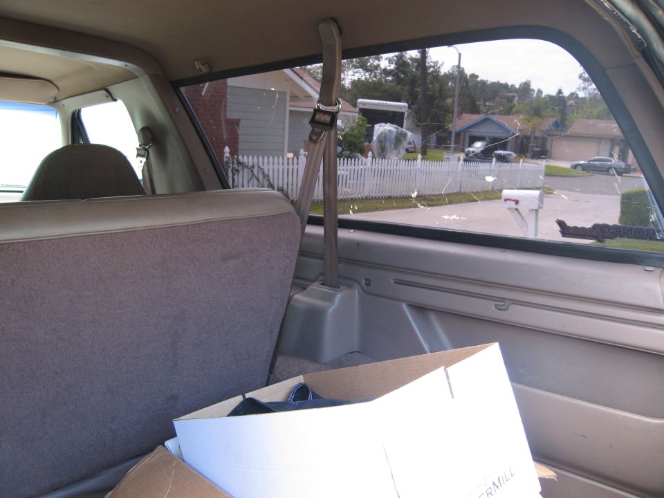 Interior rear passenger view of a Ford Bronco looking out the side window at a suburban street with a box in the foreground.
