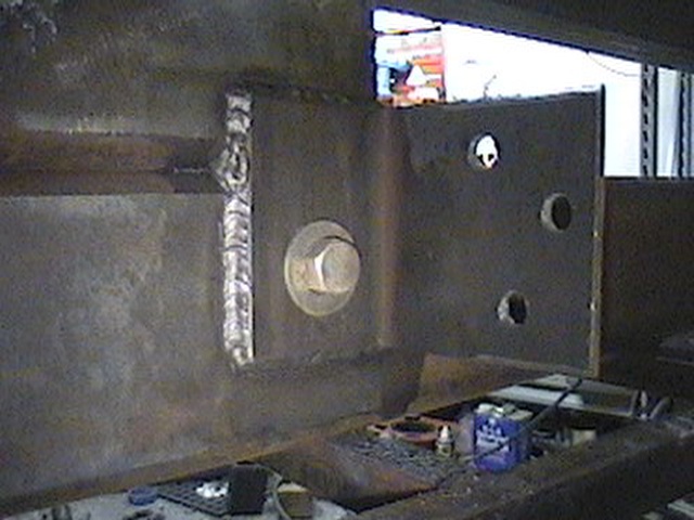 Close-up of a welded metal joint with a large bolt. Some tools and a blue container are on the surface below