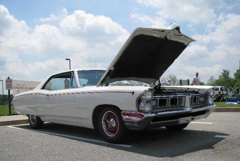White classic coupe with hood open, red-accented wheels, and side stripe.