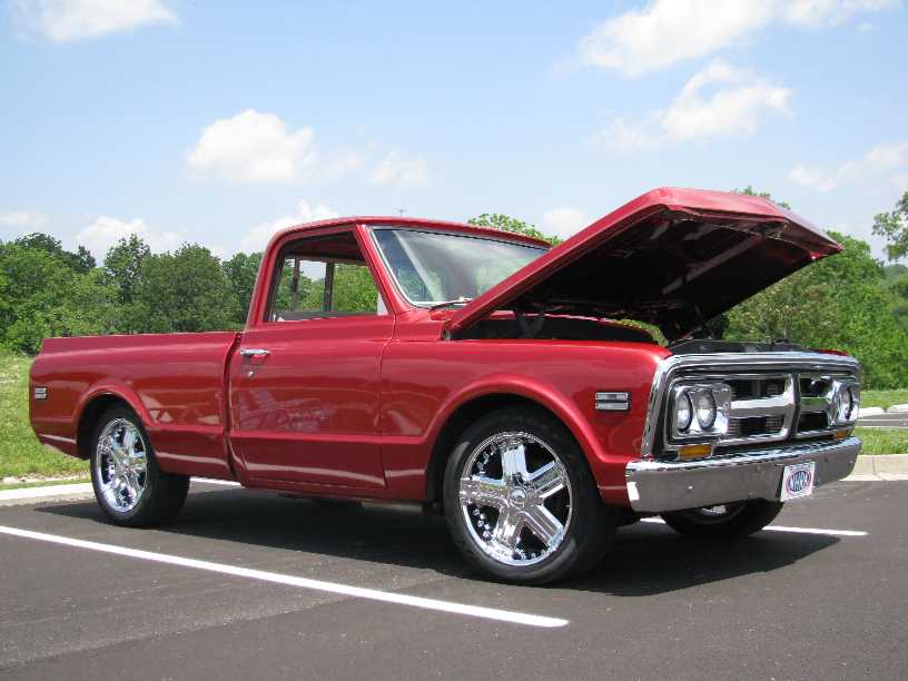 Red classic pickup truck with hood open, chrome wheels, parked in asphalt lot.