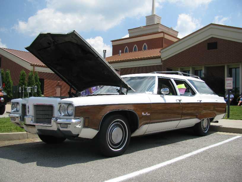 Wood-paneled station wagon, hood open, parked outside a building