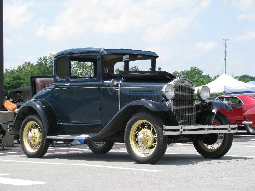 Dark blue coupe with yellow wire wheels and a chrome grille, parked outdoors
