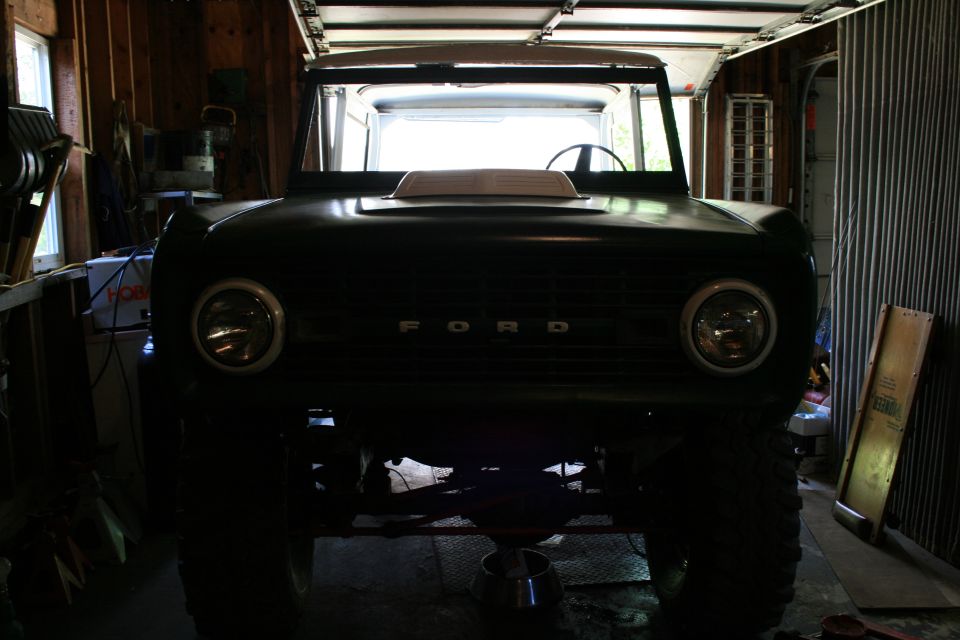 Front view of a dark 1974 Ford Bronco in a garage with a hood scoop