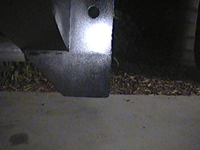 close-up of a vehicle's metal frame and bumper bracket, with some debris on the ground