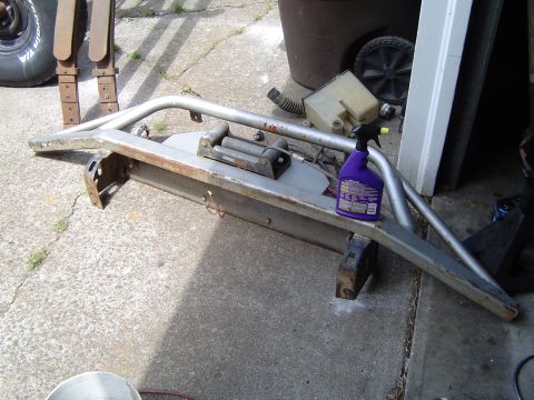1979 Ford Bronco - Aftermarket front bumper assembly with a winch, sitting on concrete. A spray bottle rests on the bumper.