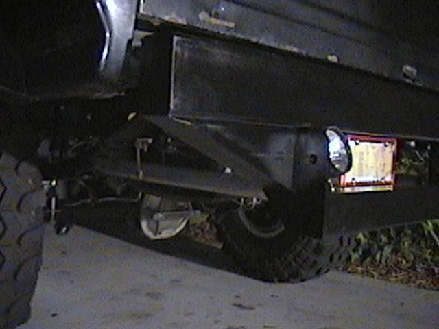 Black bumper with license plate light and license plate attached. Tire visible on left