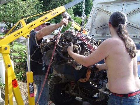 1979 Ford Bronco - Two people use an engine hoist to remove the engine from a vehicle, with the hood open.