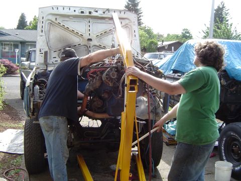 1979 Ford Bronco - An engine is being lifted out of a vehicle with the hood open, while two people operate the hoist.
