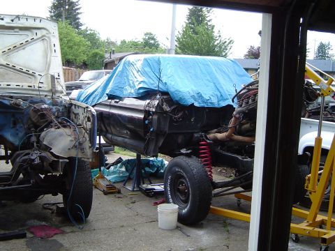1979 Ford Bronco - Two vehicles are in a state of disassembly, with one body covered by a blue tarp, revealing exposed engines and chassis components.