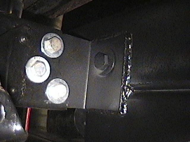 Close-up of a black metal bracket attached to a vehicle frame with three large bolts