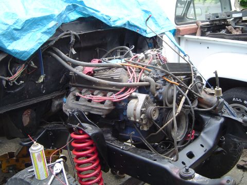 1979 Ford Bronco - The engine bay of a vehicle is partially covered by a blue tarp, with red springs and tools visible.