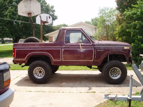1980 Ford Bronco - Side view of a maroon 1980 Ford Bronco, showing its lifted suspension and spare tire in the bed.